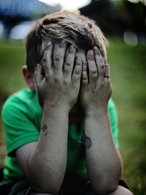 boy sitting while covering his face