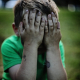 boy sitting while covering his face