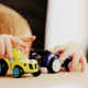 child playing with two assorted-color car plastic toys on brown wooden table