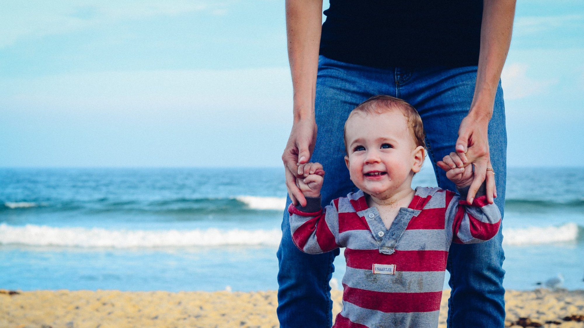 man assisting baby to walk on beach