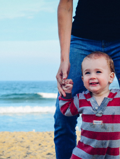 man assisting baby to walk on beach